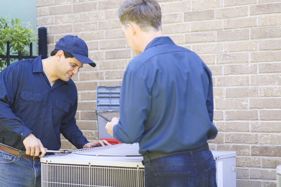 Two individuals repair an outdoor air conditioning unit.