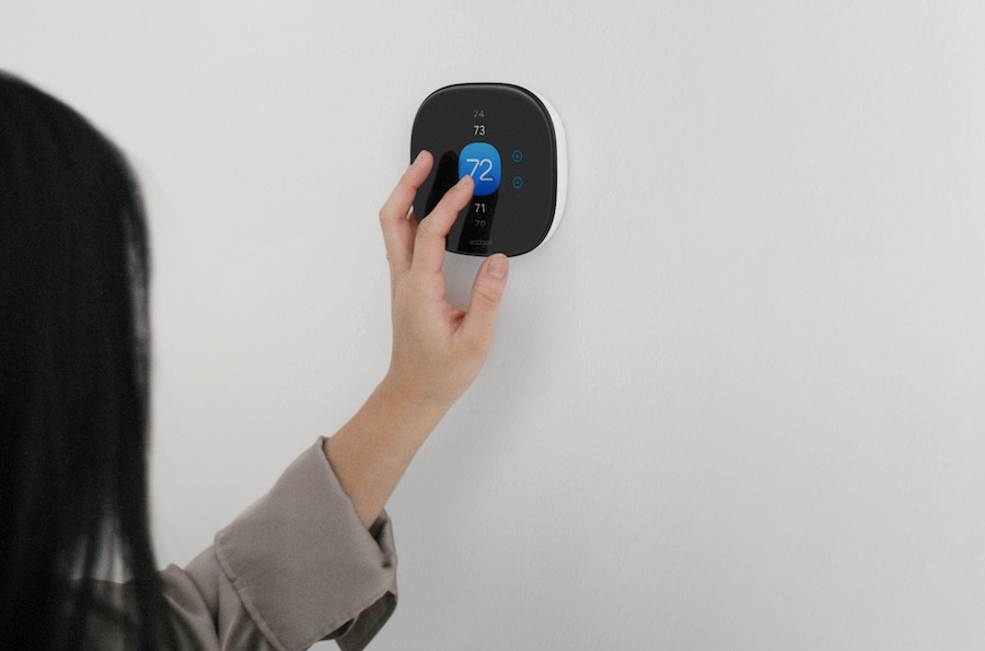  Women touching an Ecobee smart thermostat on the wall. 