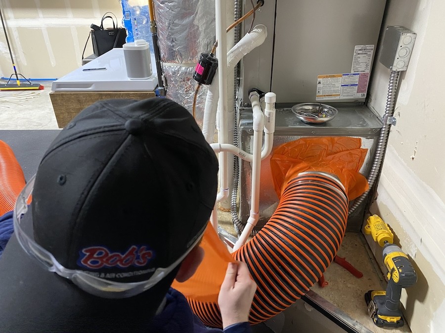 Someone in a Bob’s Heating hat cleaning an air duct system with a large vacuum tube.