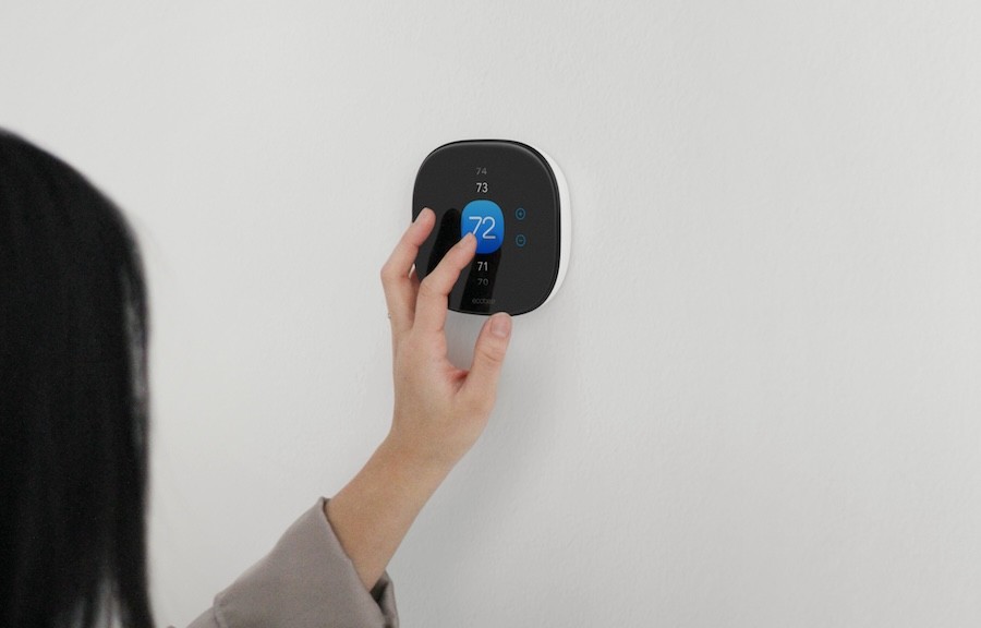 Woman tapping a smart thermostat on the wall. 